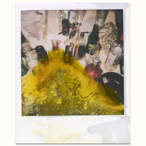 White frame Polaroid Instant Film 600 with lime green liquid and chemical deterioration from the bottom featuring dirty table with alcohol containers.